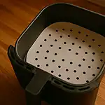 Perforated parchment paper placed safely inside air fryer basket before cooking, under warm light.